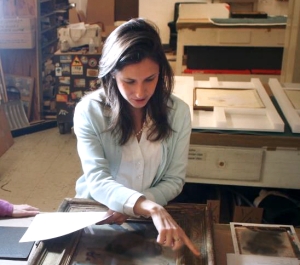 Seated woman pointing at a picture frame.